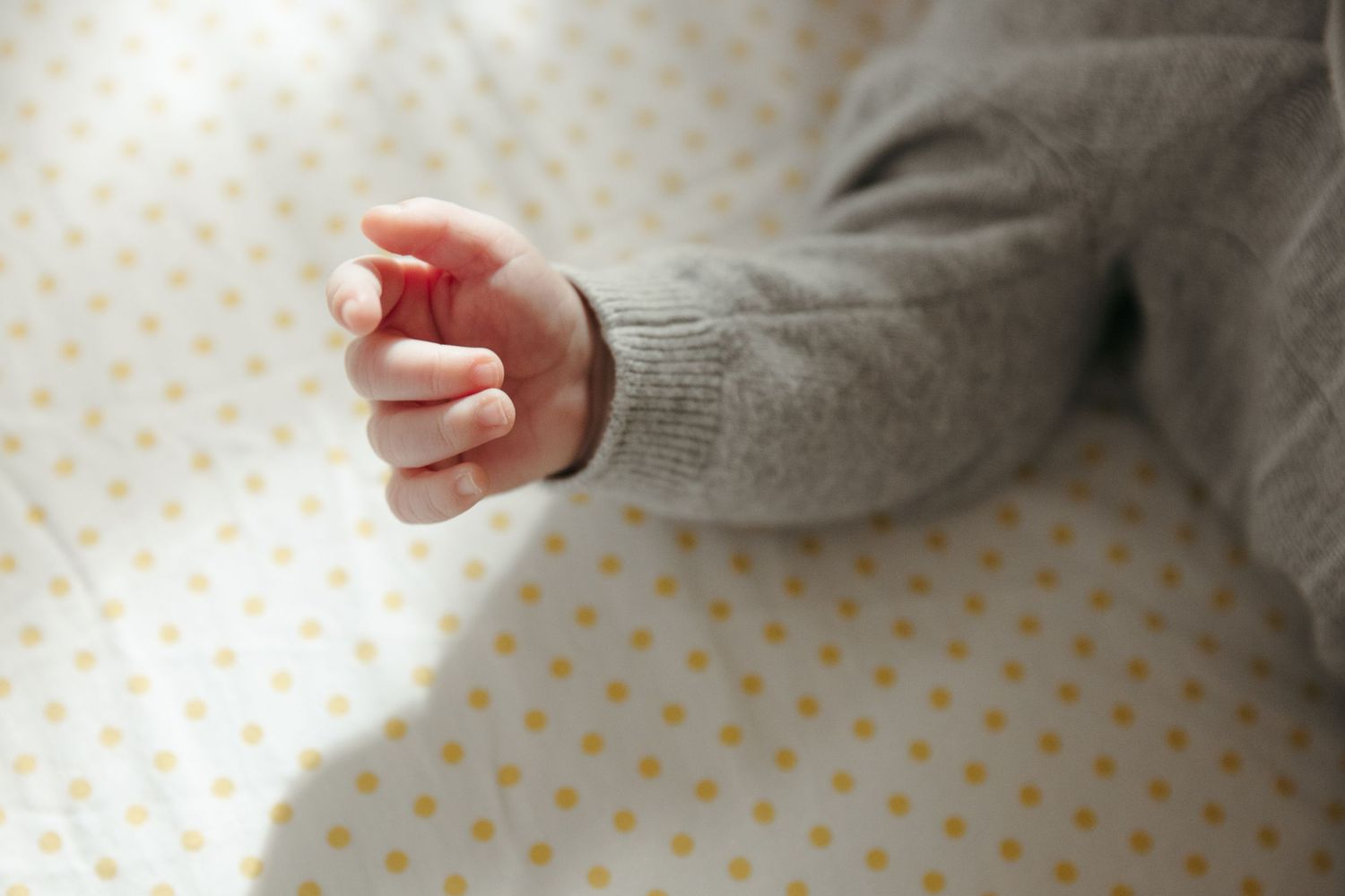 Sweet intimate moment with a newborn baby wrapped in a cozy gray knit blanket.