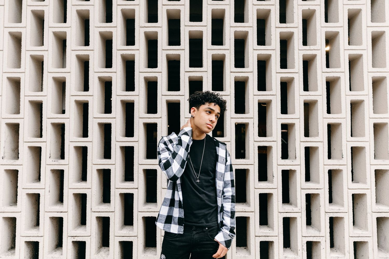 Person in streetwear poses against geometric white architectural wall pattern.