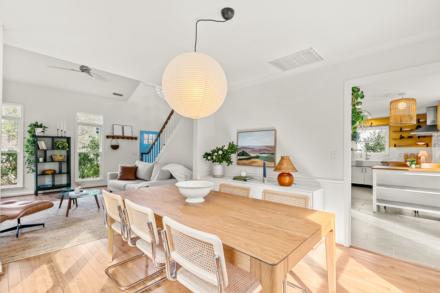 Bright open-plan dining room with wooden table, white chairs, globe pendant light, and modern living area on light hardwood floors.