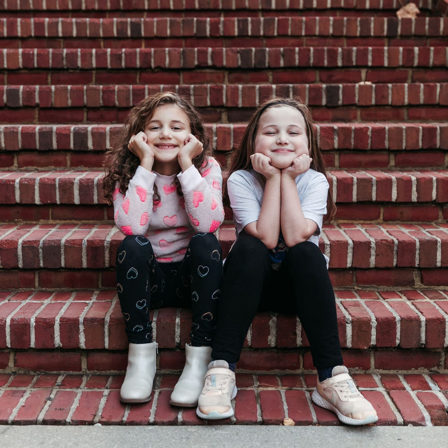 Two children sitting on brick steps making silly faces at the camera.