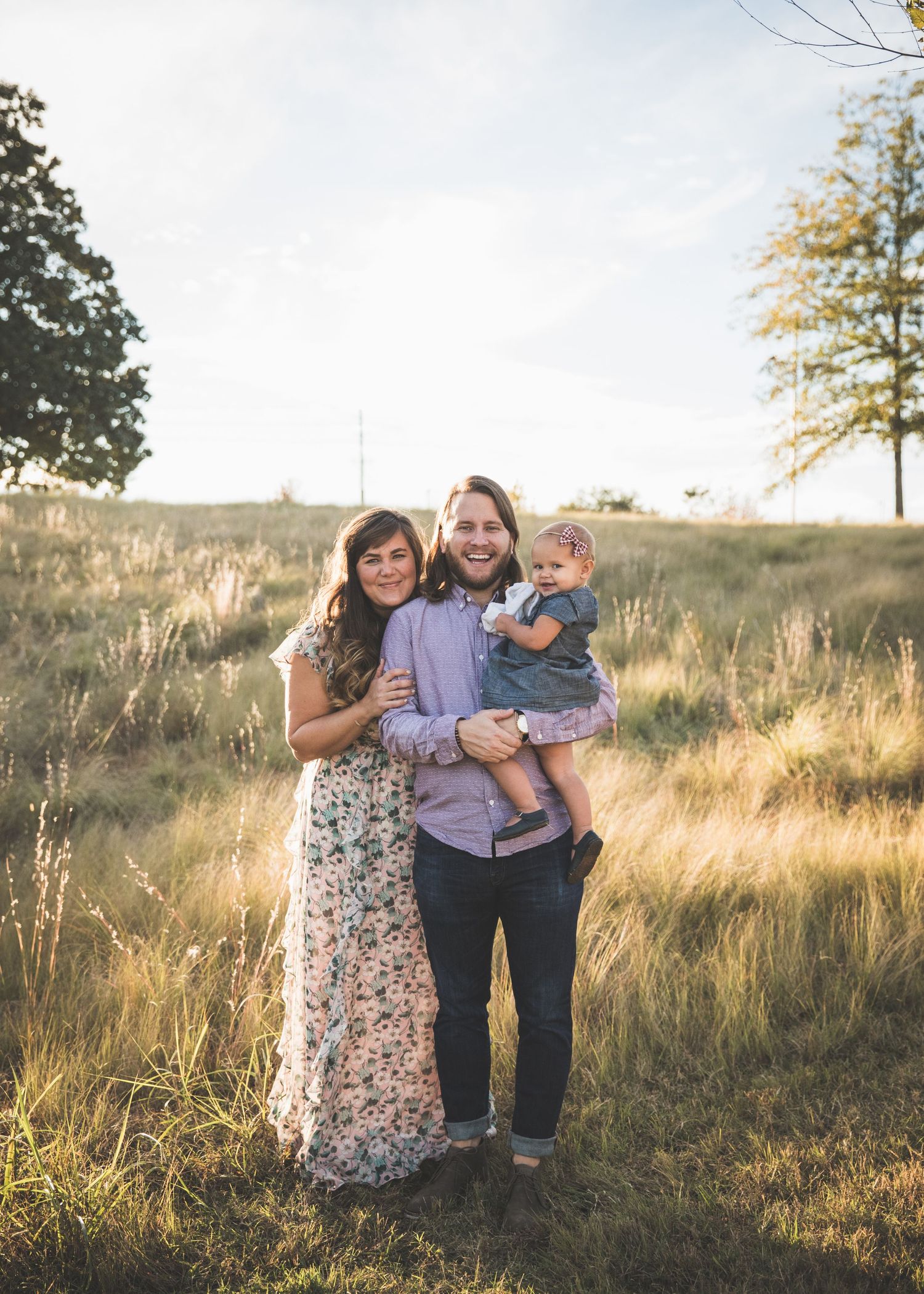 A family stands together in a golden grassy field at sunset with trees in the background.