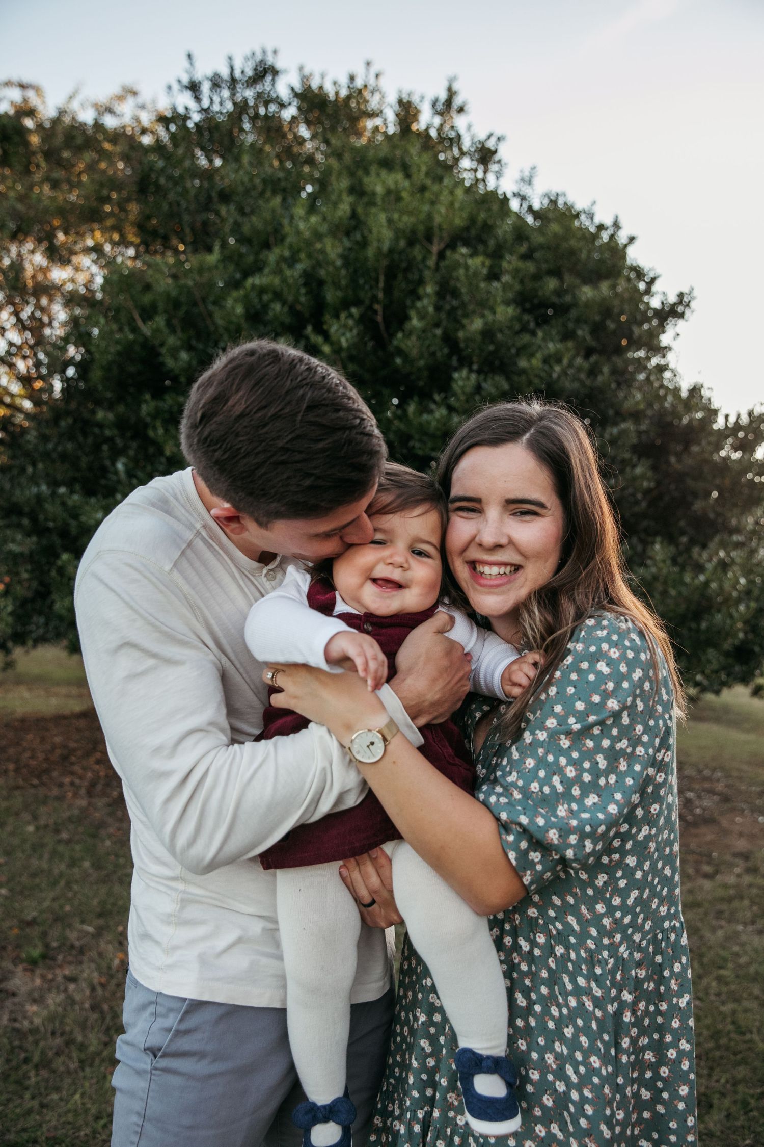 Family shares intimate moment of laughter and cuddles outdoors at dusk.