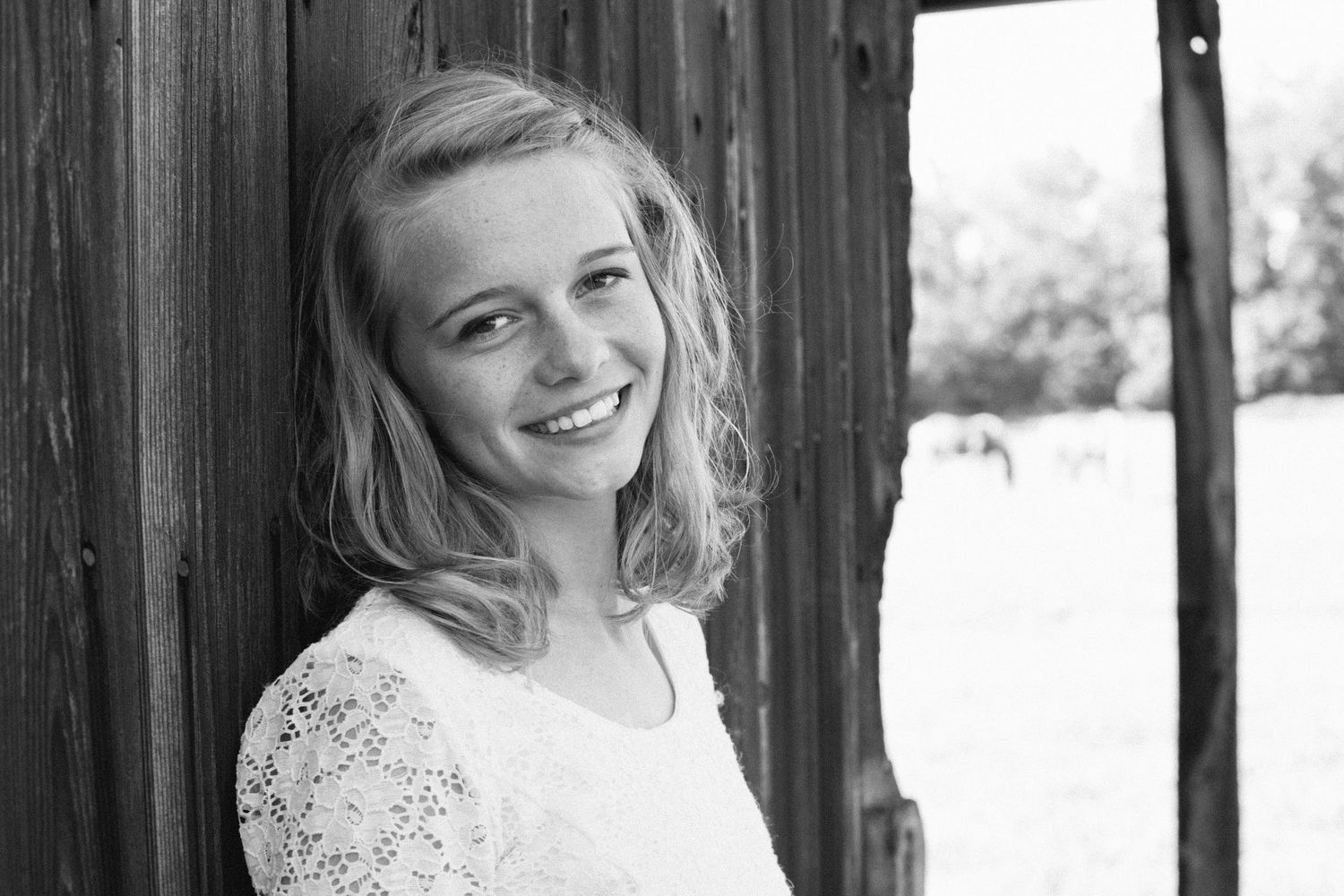 Black and white portrait of person in lace top near wooden structure.