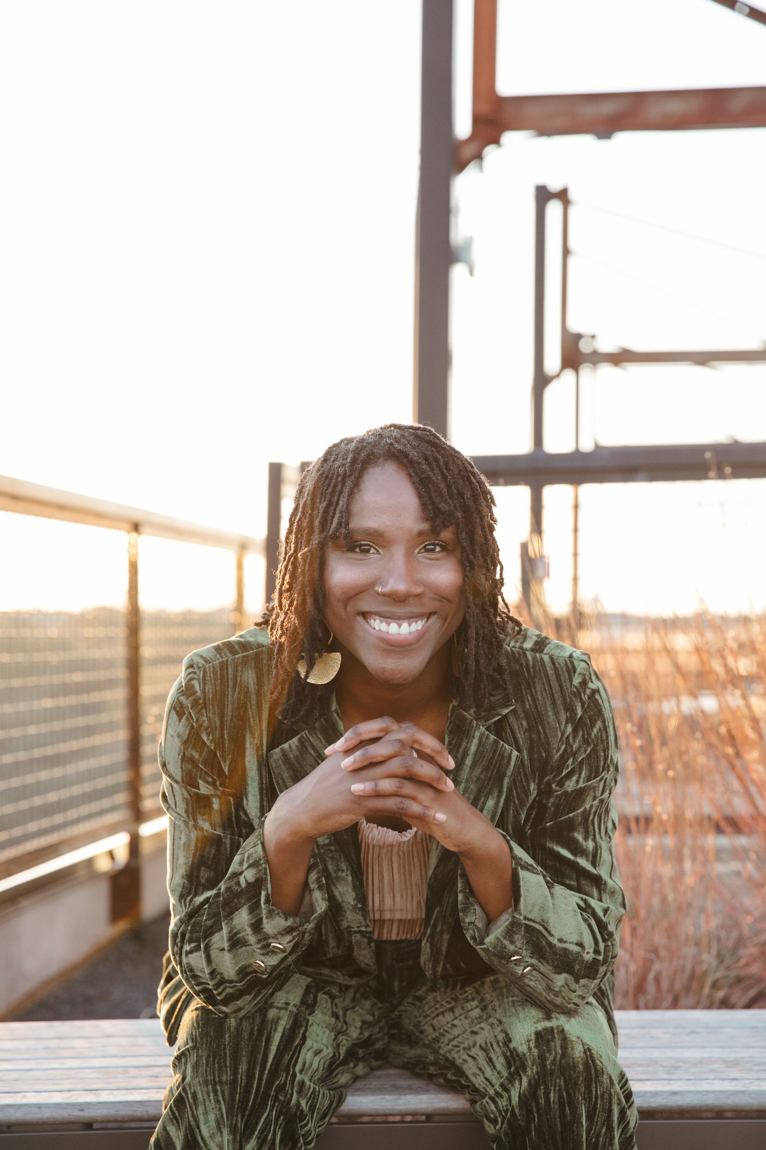 Person in green velvet outfit laughs while sitting on outdoor deck during sunset.