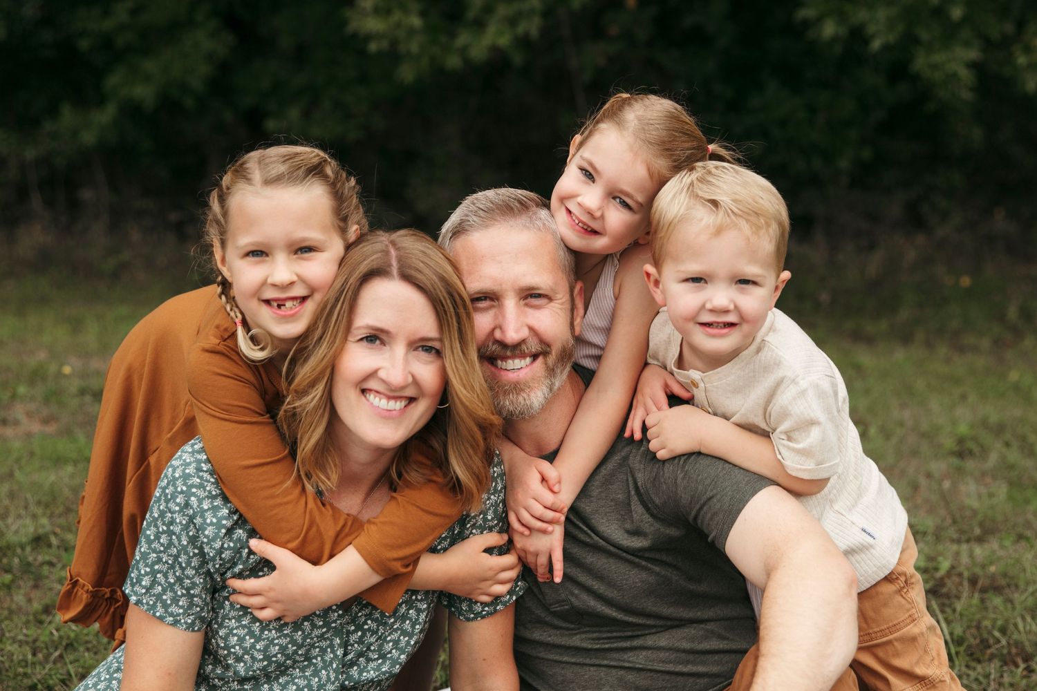 A cheerful family portrait shows loved ones hugging and smiling together outdoors.