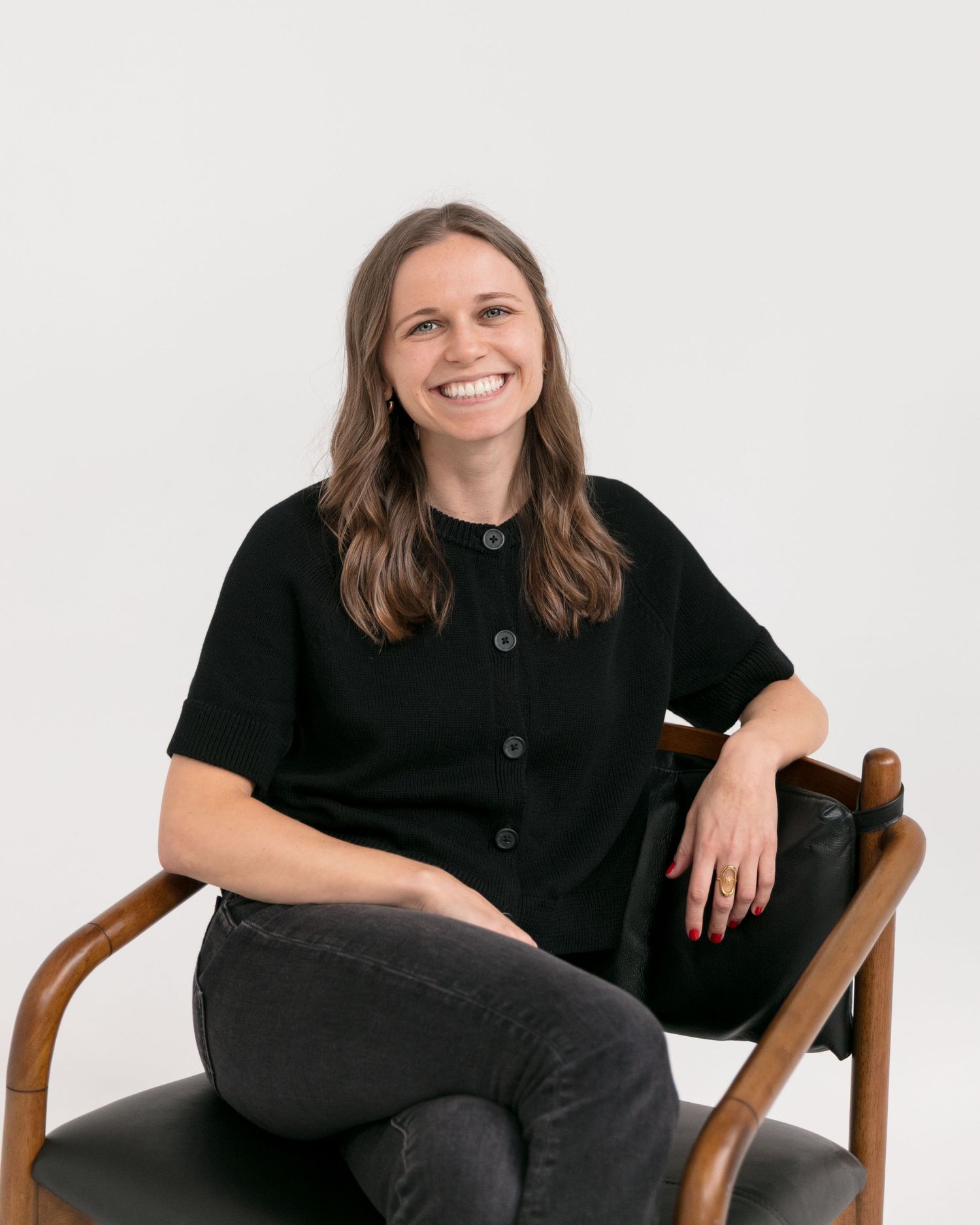 A person in black clothing sits casually in a wooden chair against a white background in four similar poses.