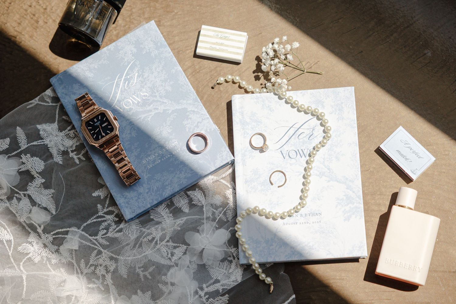 Elegant wedding flat lay with pearl necklace, gold watch, rings, and stationery.