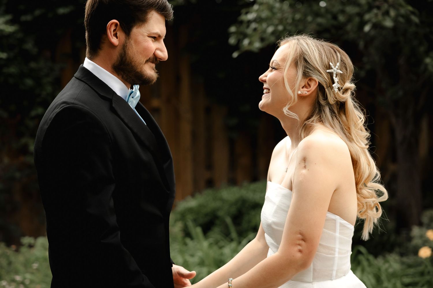 Joyful bride in white dress laughing with groom during outdoor wedding first look.