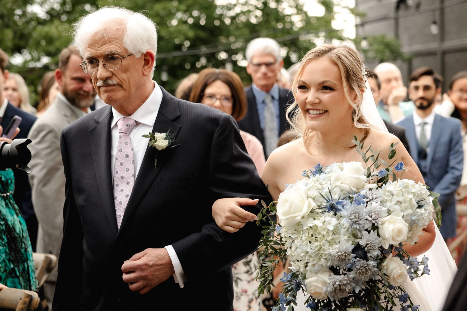 Father proudly walks bride down the aisle at an outdoor wedding ceremony.