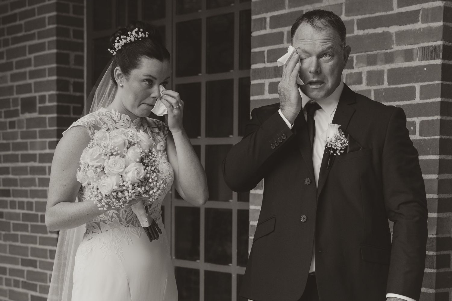 Emotional black and white photo of a bride and father crying together on wedding day.