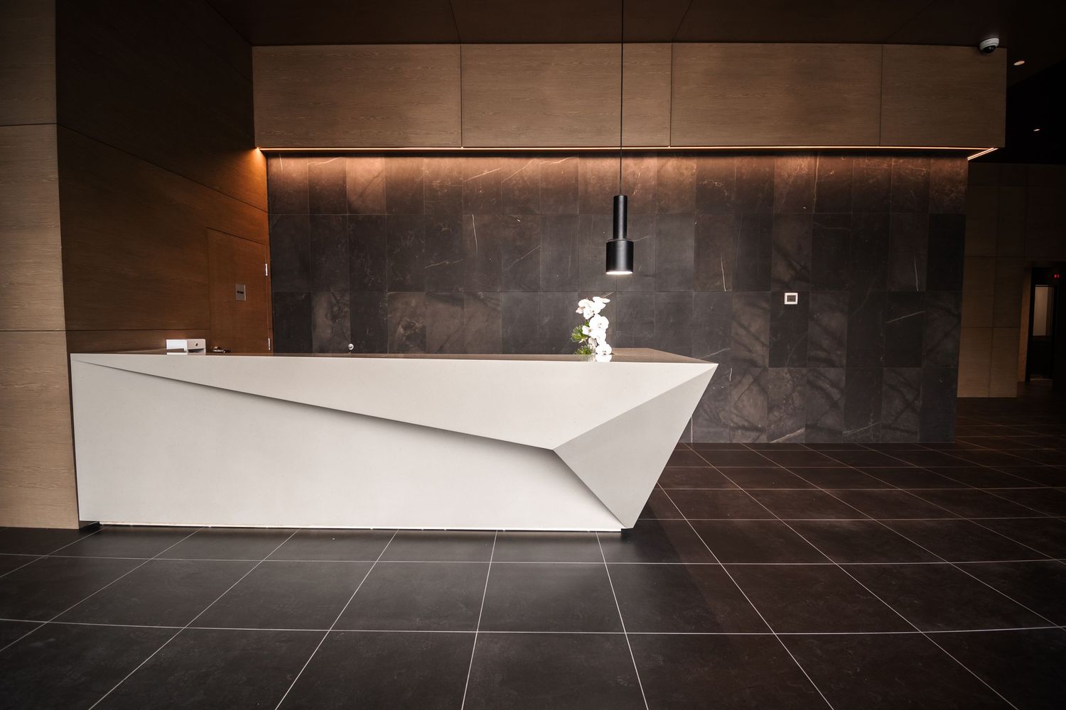 Modern minimalist white geometric reception desk in a sleek, dark-toned lobby interior.