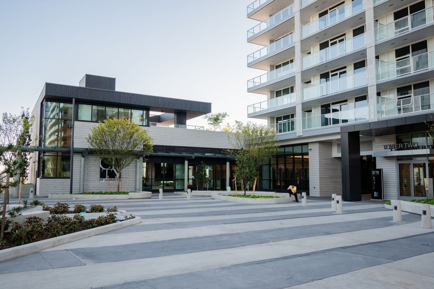 Contemporary apartment building exterior with landscaped courtyard, glass lobby entrance, and high-rise tower.