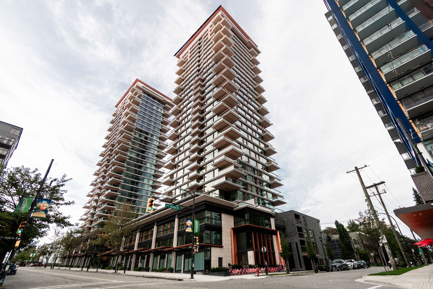 Modern high-rise condominium tower with glass balconies at a city street intersection.