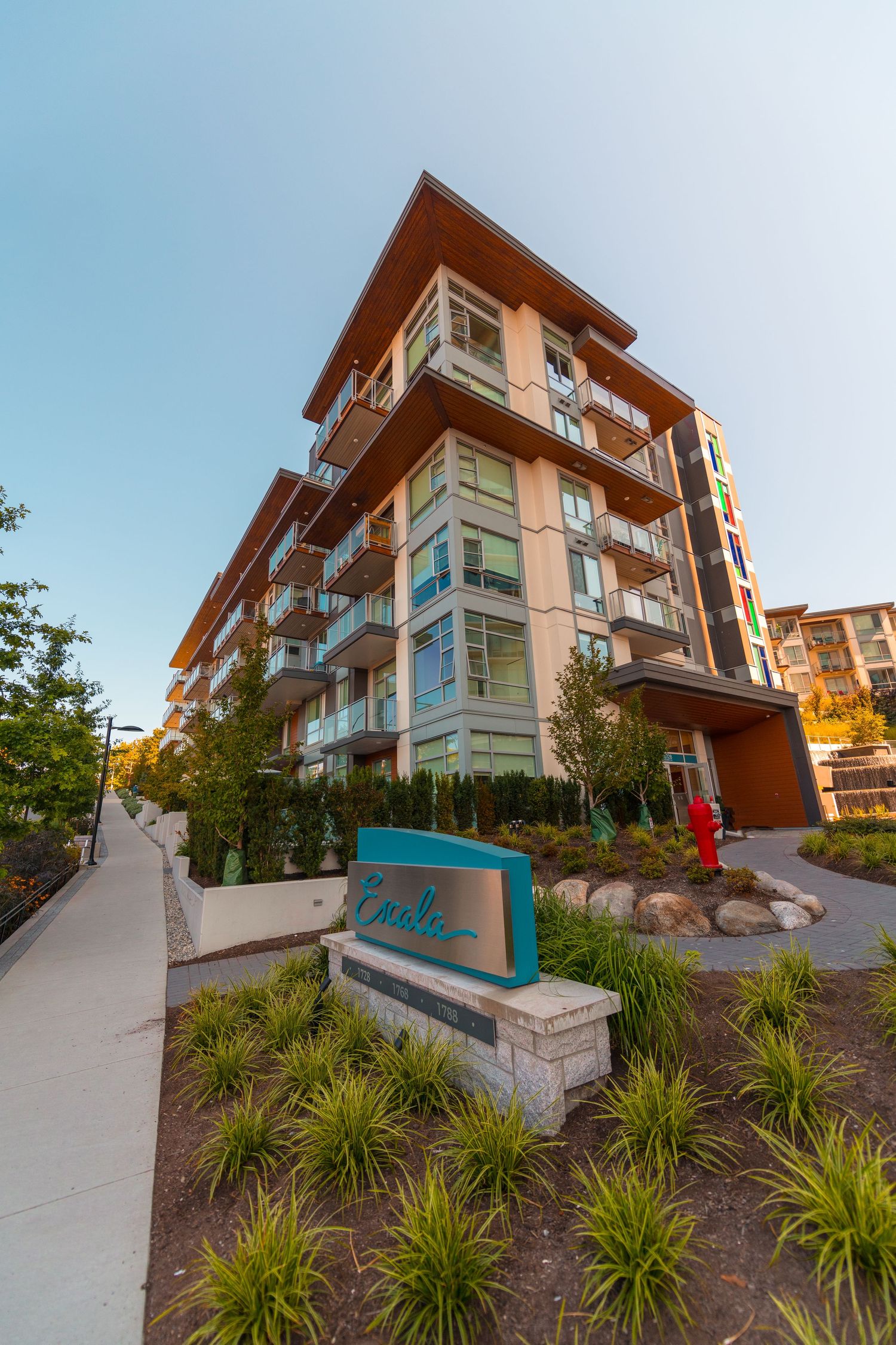 Low-rise modern apartment building with wood accents and balconies beside a landscaped entrance sign.