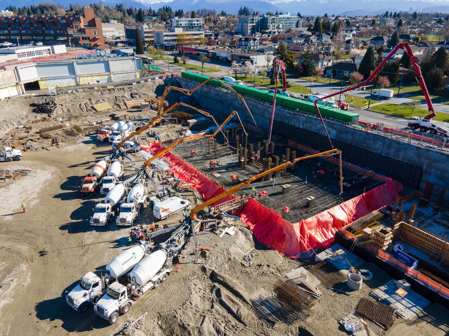 Aerial view of a large concrete construction site with cement trucks and pump booms active on a sunny day.