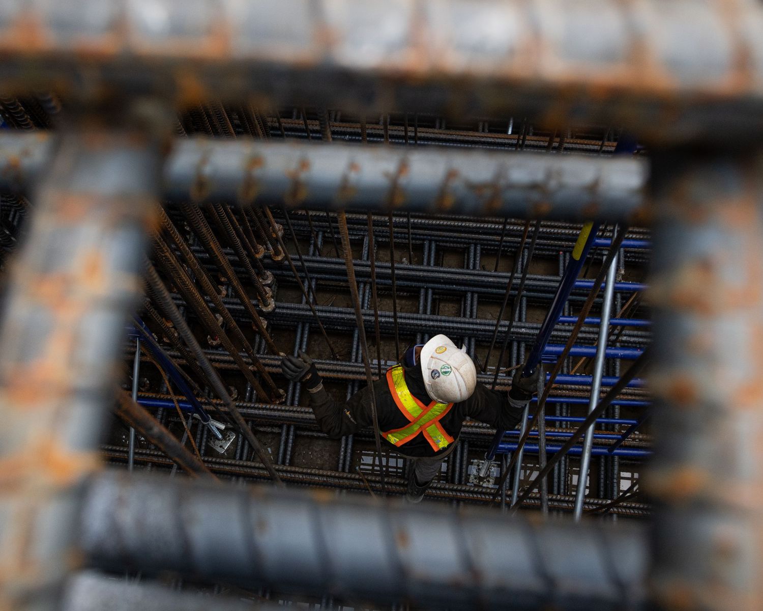 Worker in a hard hat seen through a framed opening surrounded by steel rebar at a construction site.