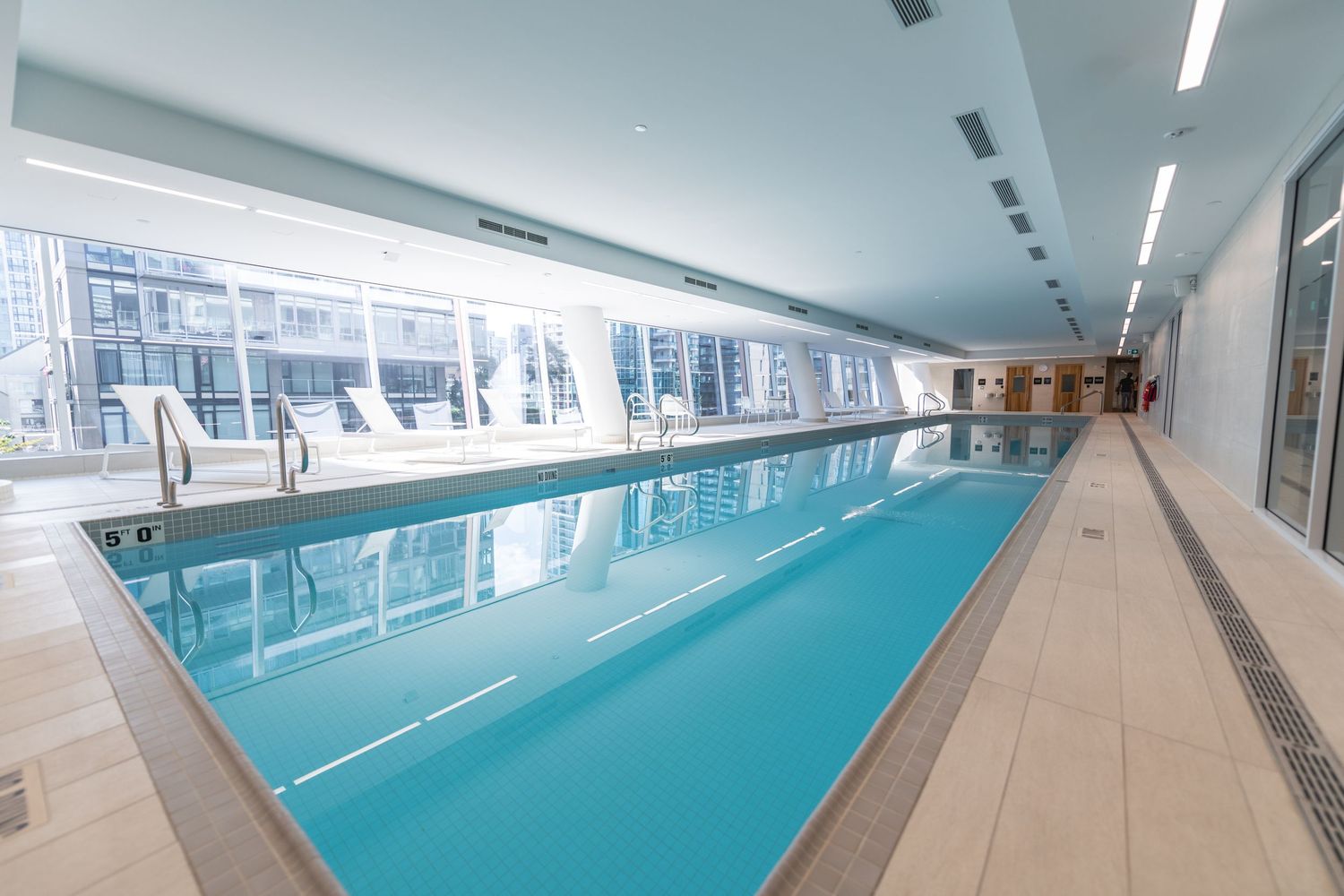 Indoor lap pool with turquoise water and floor-to-ceiling windows in a modern luxury residential building.