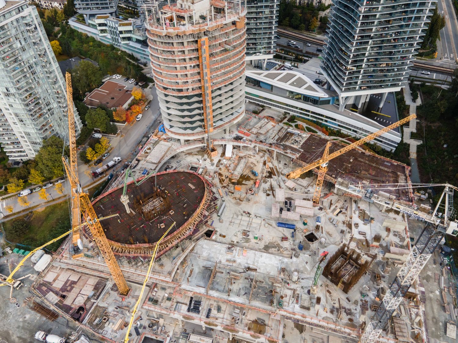 Aerial view of a large construction site with cranes and a circular concrete foundation structure.