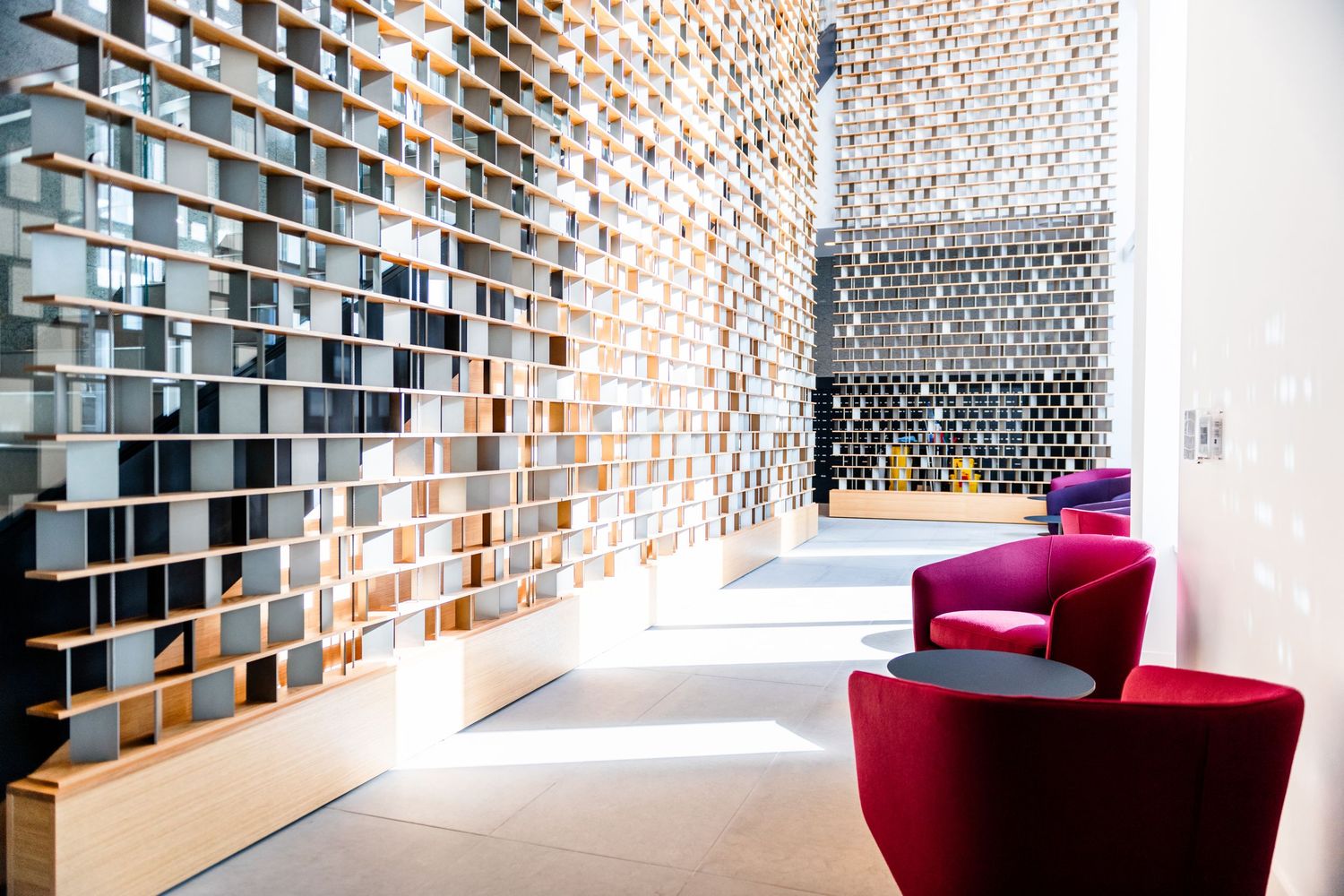 Modern building interior featuring a floor-to-ceiling geometric wood and mirror decorative wall with red chairs.