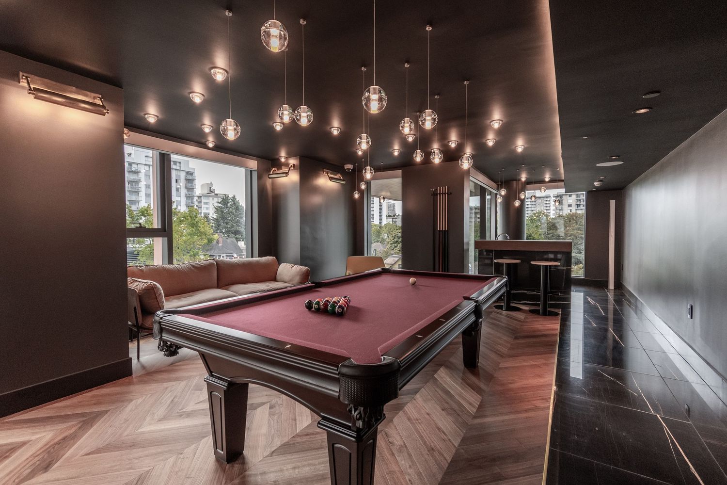 Elegant billiard room with pendant lighting, red felt pool table, and herringbone wood floors.
