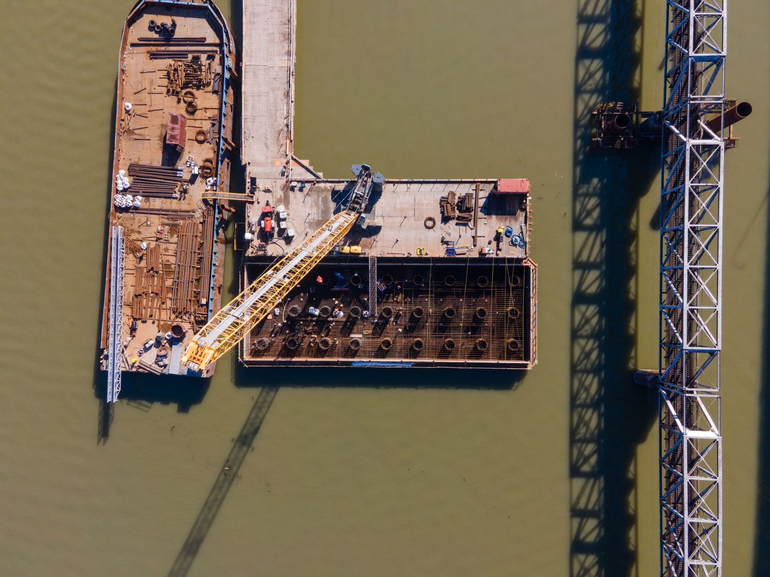 Aerial view of a construction barge with pile foundations in murky green river water.