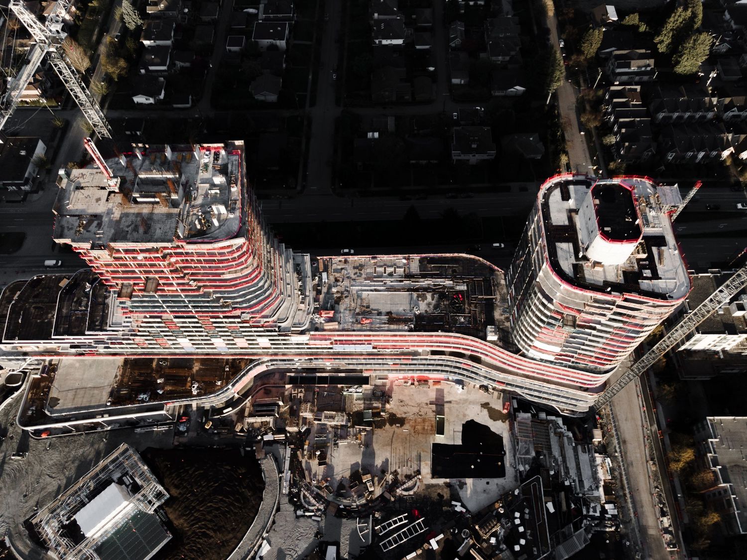 Bird's eye aerial view of two curved high-rise buildings under construction in an urban city block.
