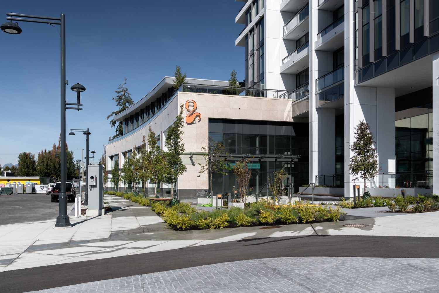Modern mixed-use building exterior with curved facade, landscaped plaza, and decorative street signage.