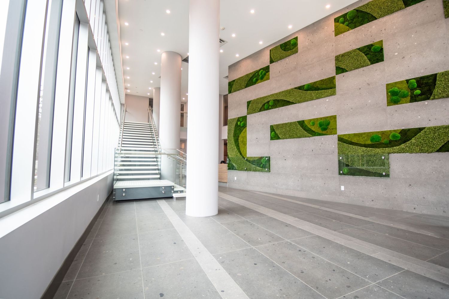 Bright contemporary building lobby with green moss wall art and glass staircase.