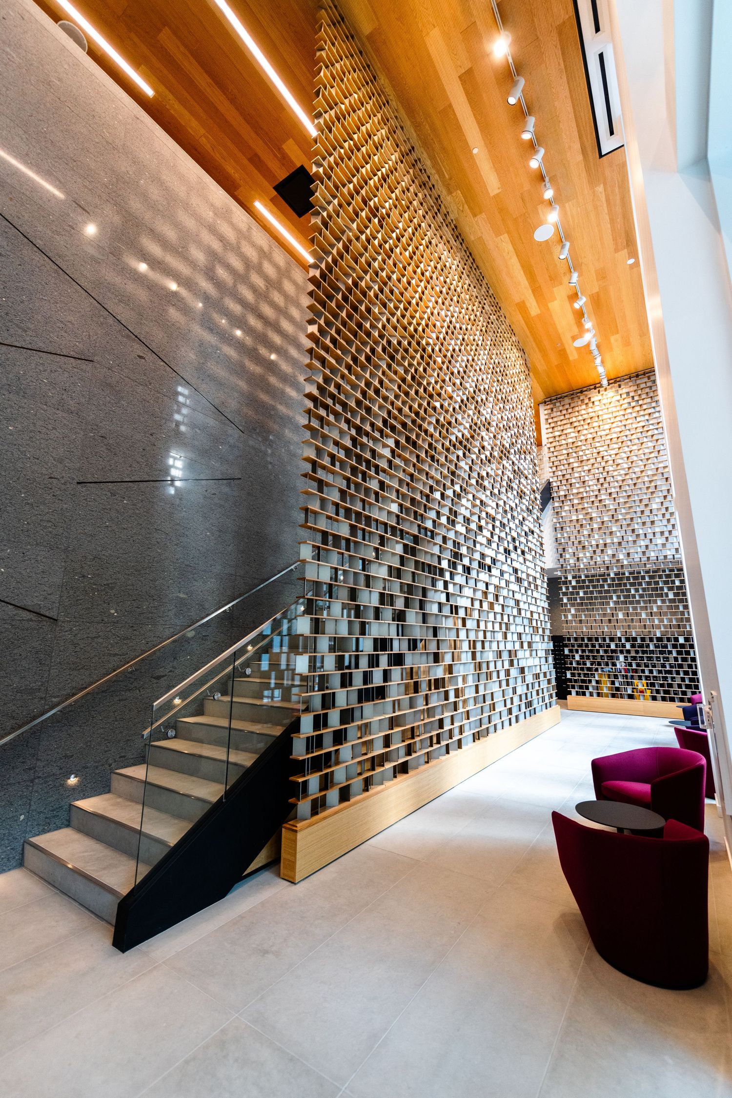 Modern lobby staircase with a dramatic textured mosaic feature wall and warm wooden ceiling accents.
