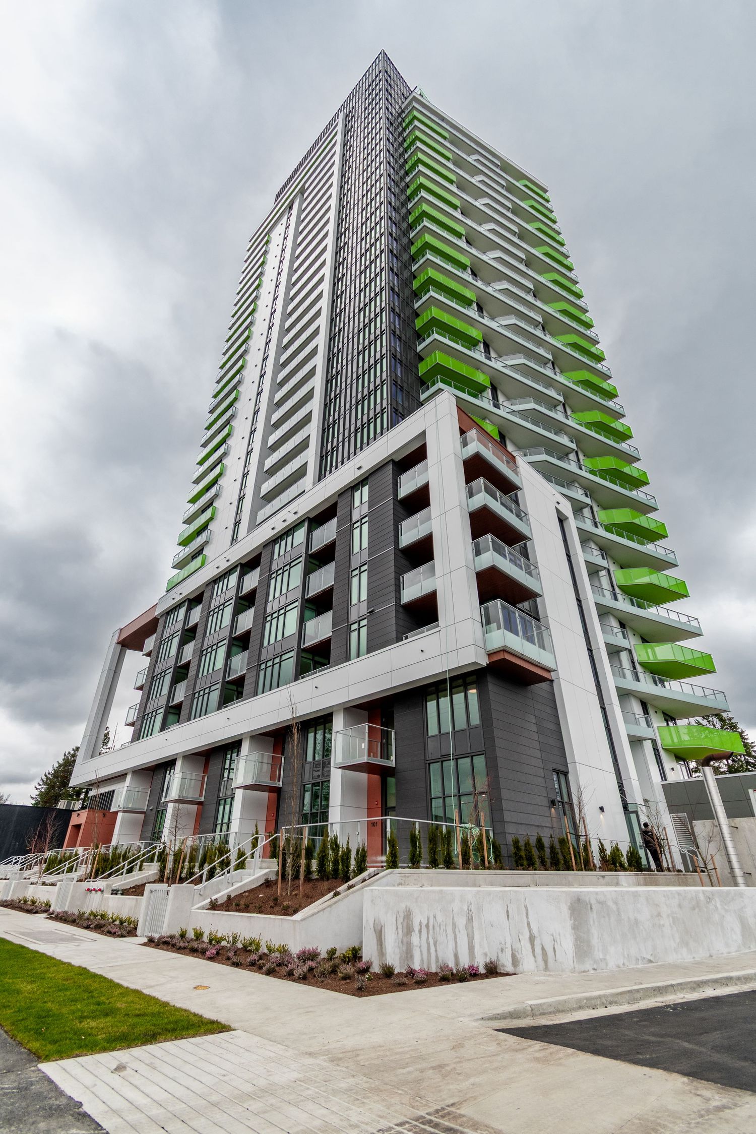 Tall modern residential tower with distinctive green balconies against a cloudy sky.