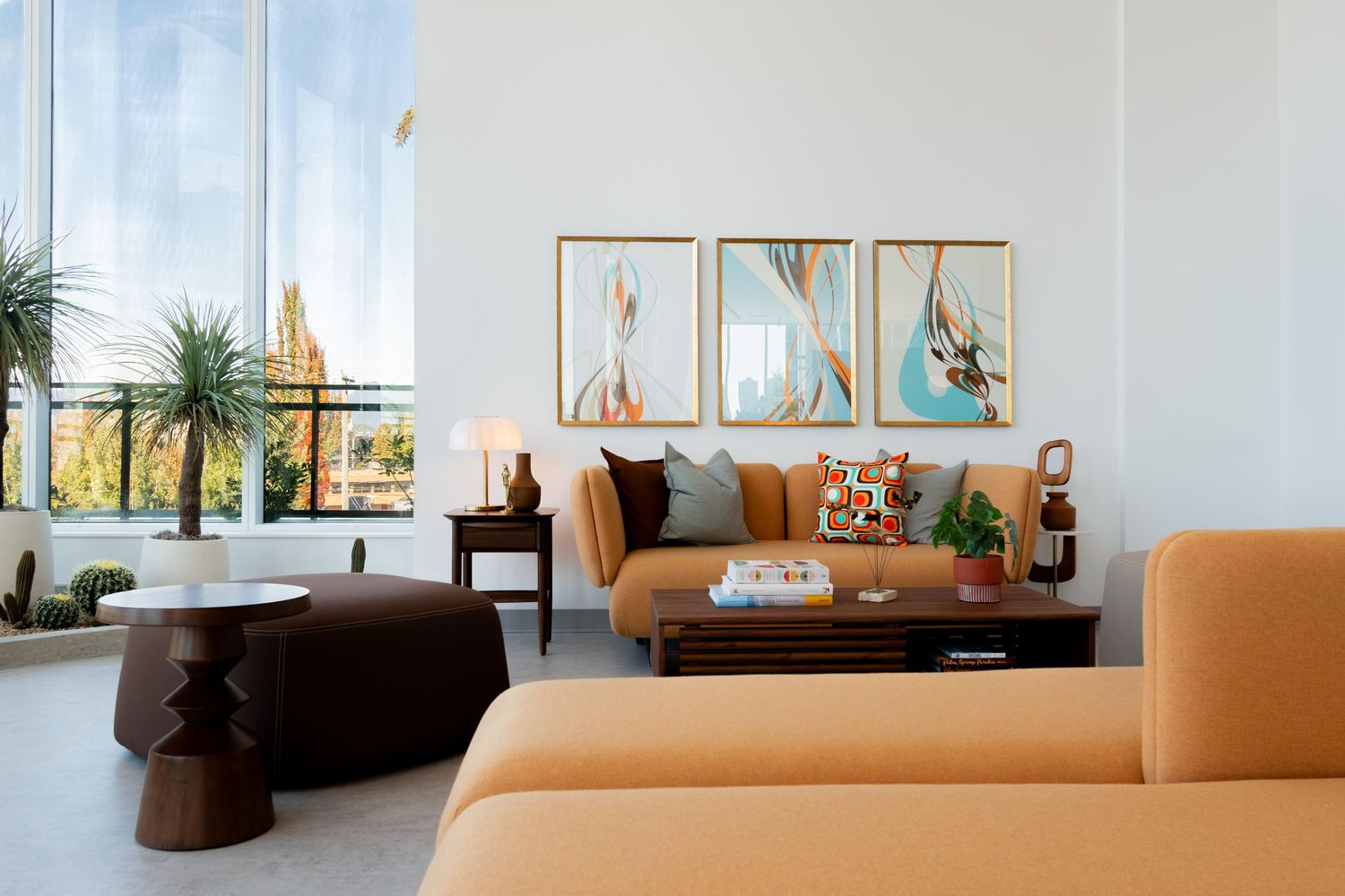 Modern living room with orange sofas, wood coffee table, and abstract triptych artwork on white walls.