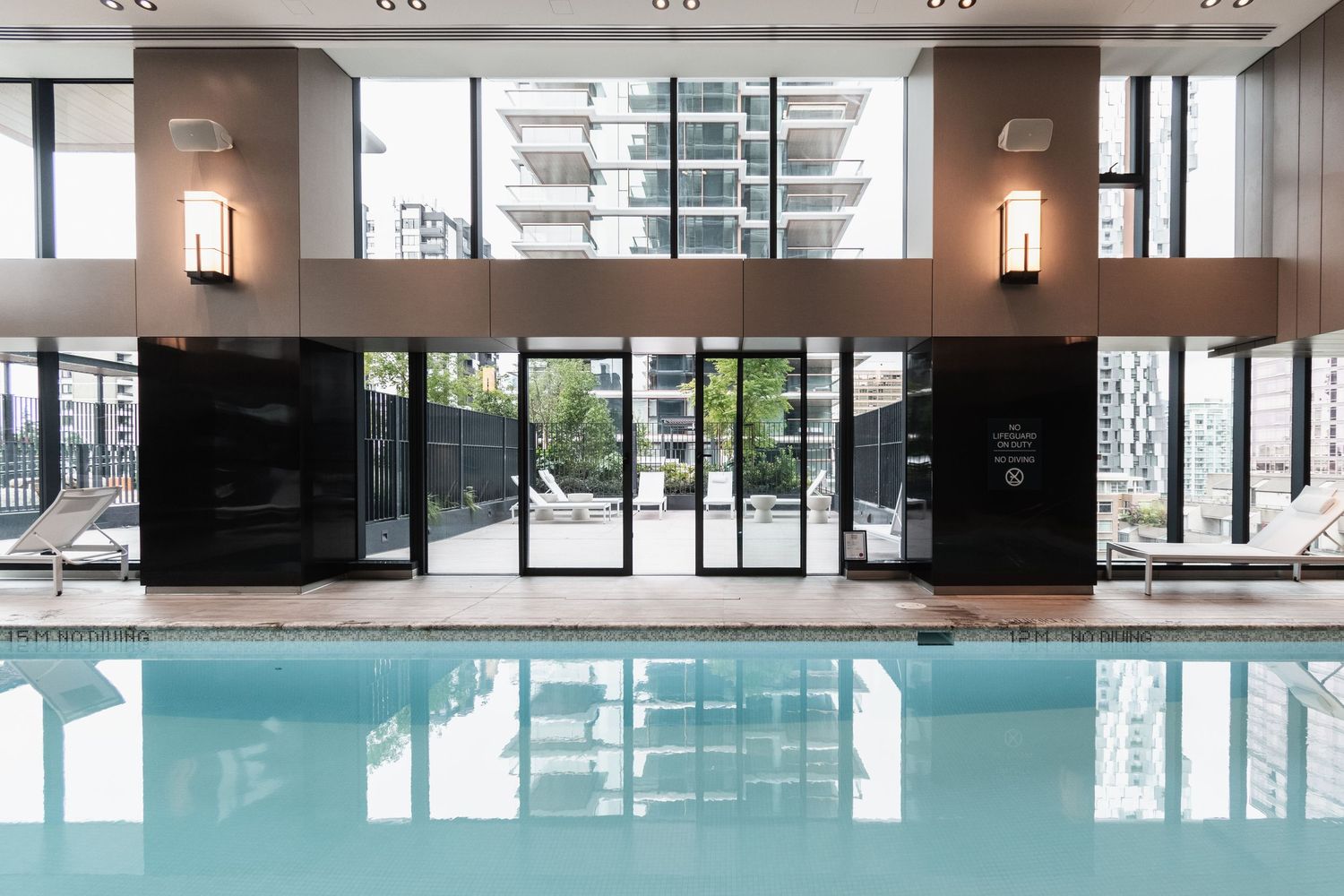 Modern indoor swimming pool with floor-to-ceiling windows and city views in a luxury building.
