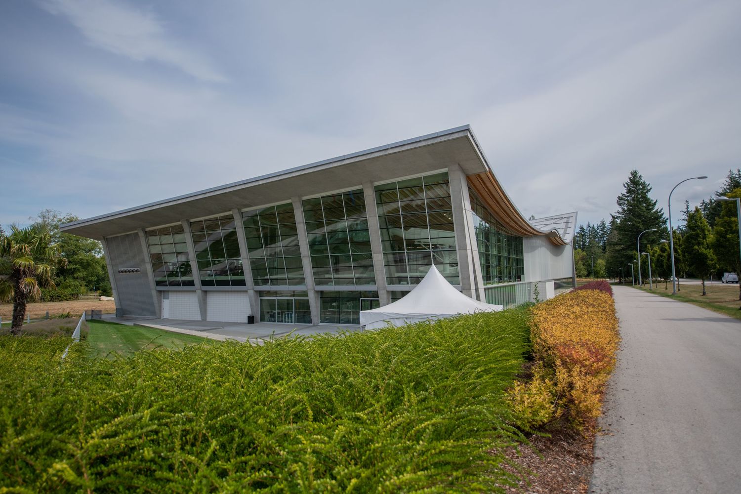 Modern glass and wood community building surrounded by lush greenery under a partly cloudy sky.