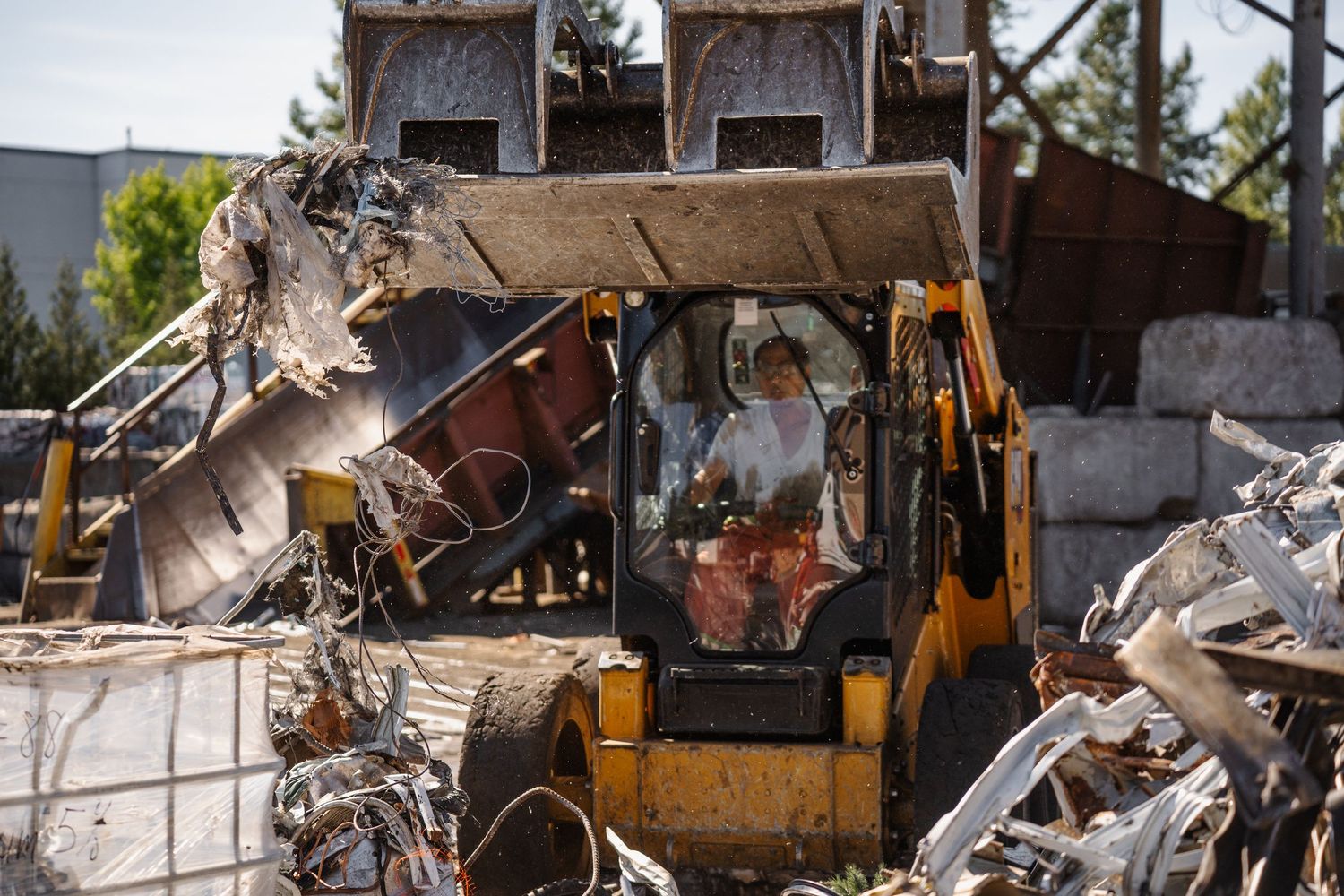 Worker operating yellow excavator machinery amid large pile of demolition debris and scrap metal outdoors.