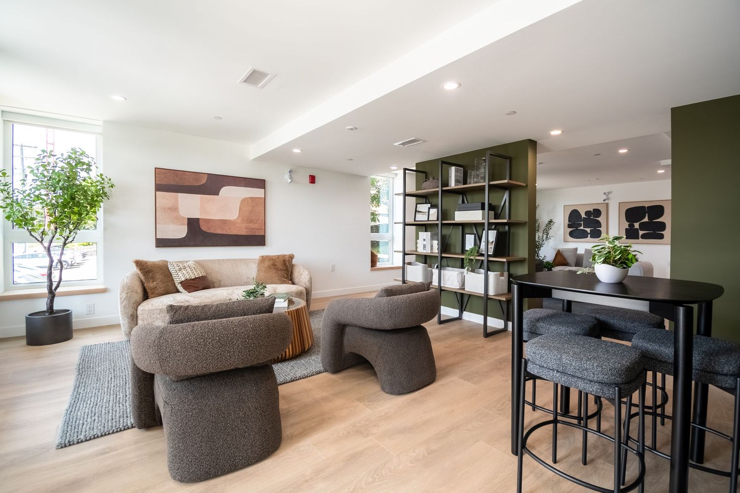 Modern apartment living room with neutral tones, a green accent wall, bookshelf, and light hardwood floors.