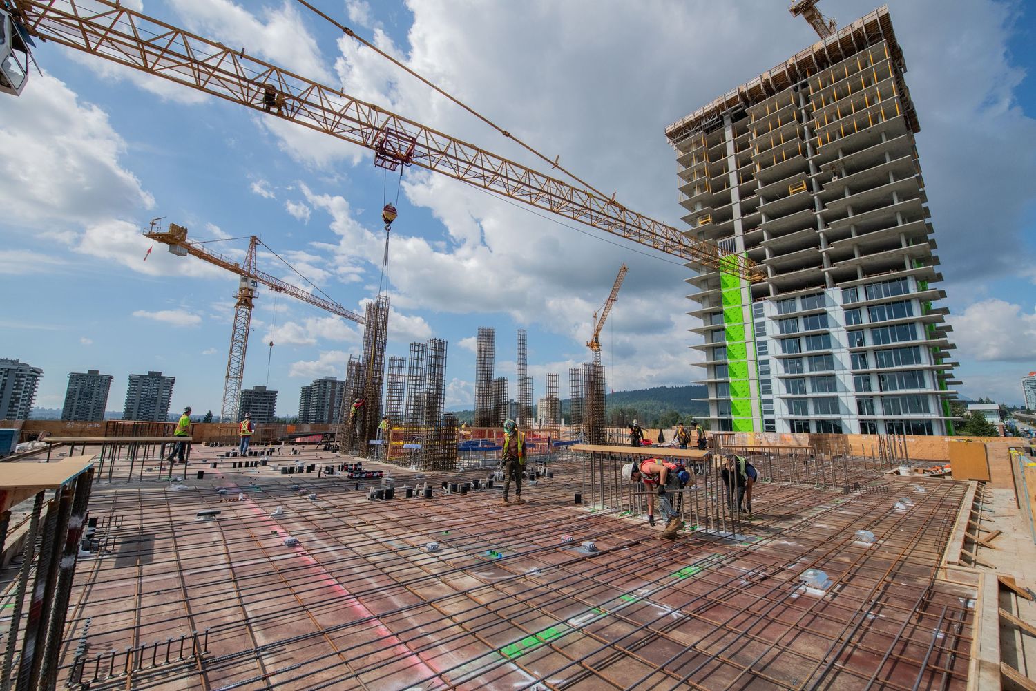 Aerial view of a large concrete construction site with cranes and a partially built high-rise tower.