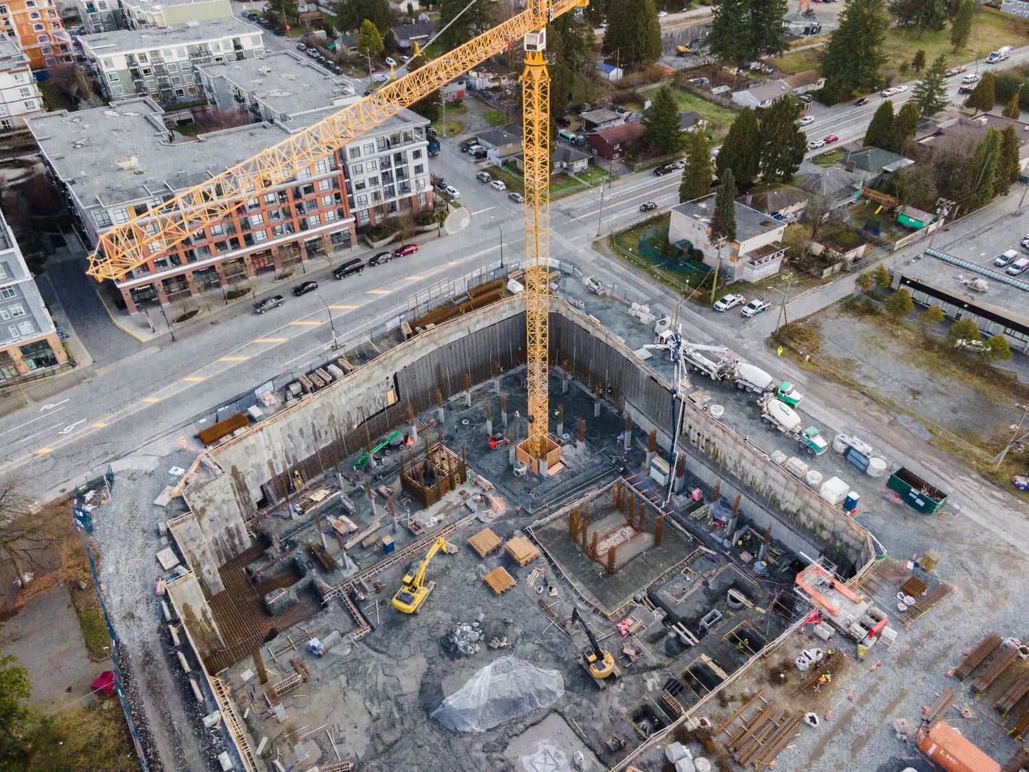 Aerial view of a large urban construction site with a yellow tower crane and deep foundation excavation.