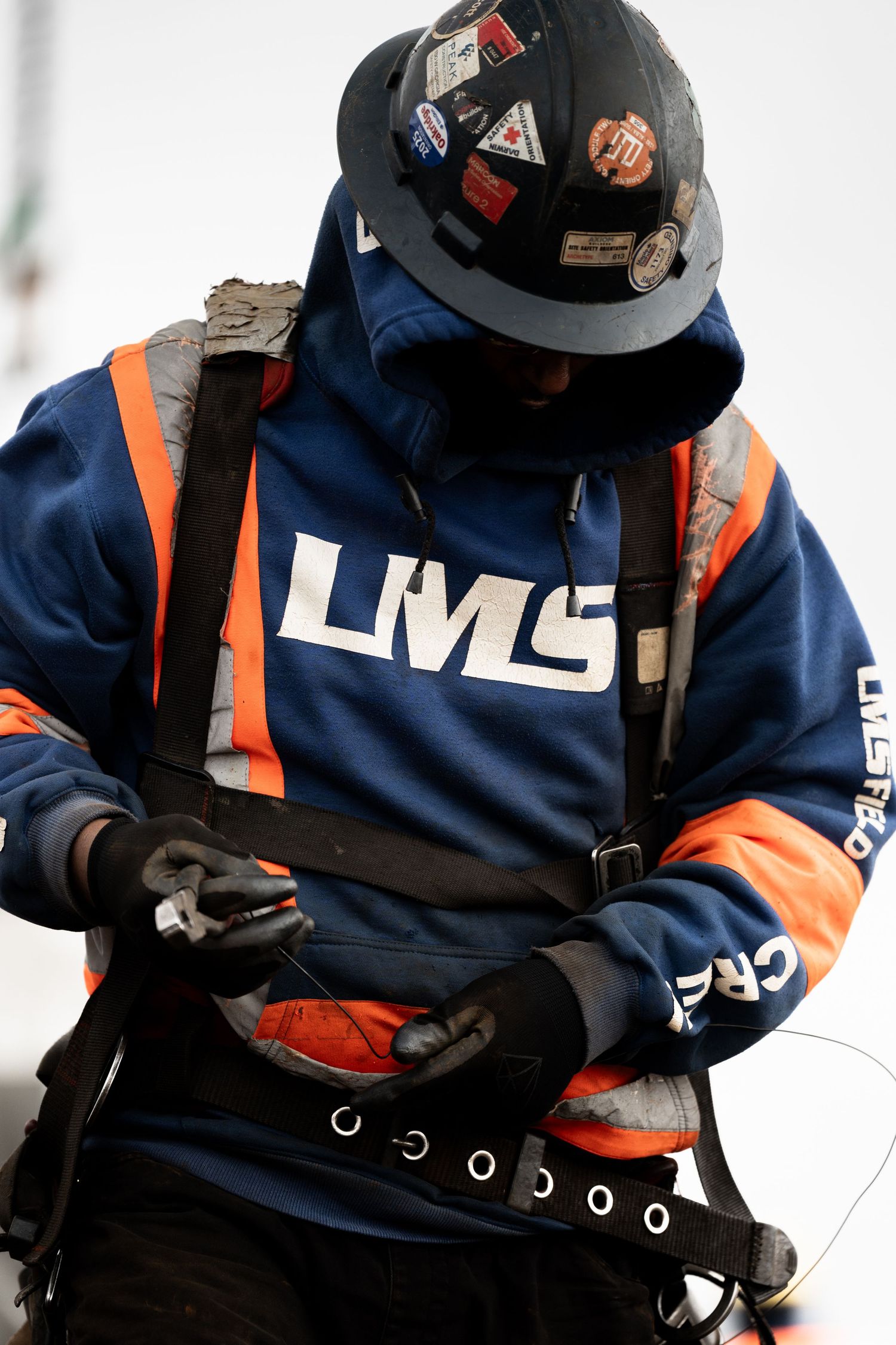 Construction worker in LMS hoodie, hard hat, and safety harness working on a high-rise building site.