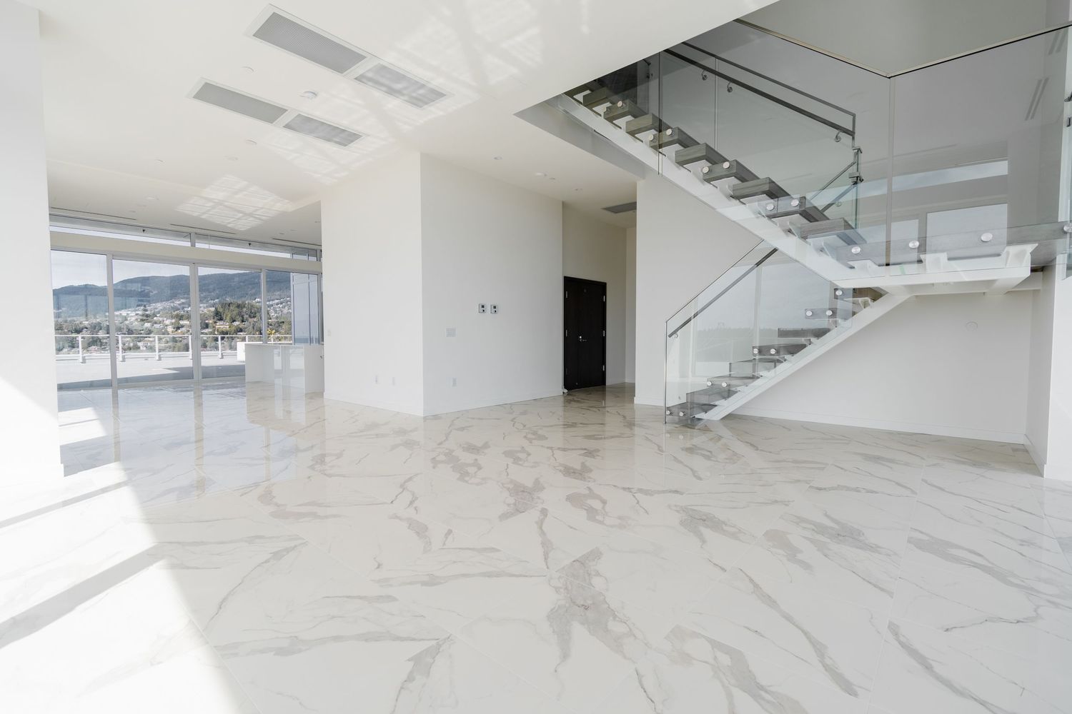 Bright open-plan interior with white marble floors and glass staircase in a luxury penthouse unit.