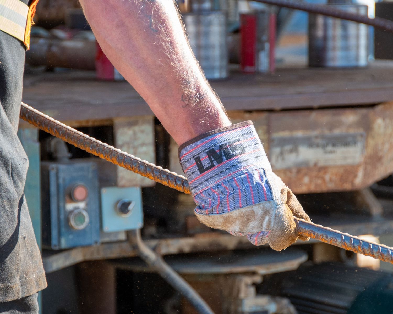 Close-up of a gloved construction worker gripping a steel rebar rod with LMC-branded wrist support.
