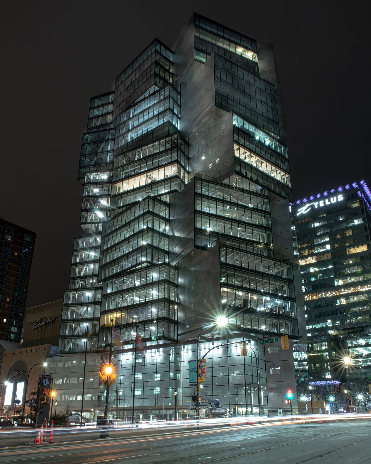 Illuminated glass office tower at night with light trails from passing traffic below.