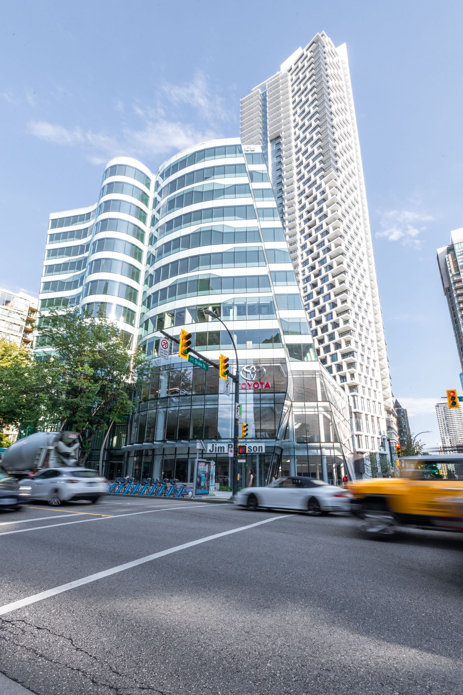 Street-level view of curved glass building and modern skyscraper with traffic in downtown Vancouver.