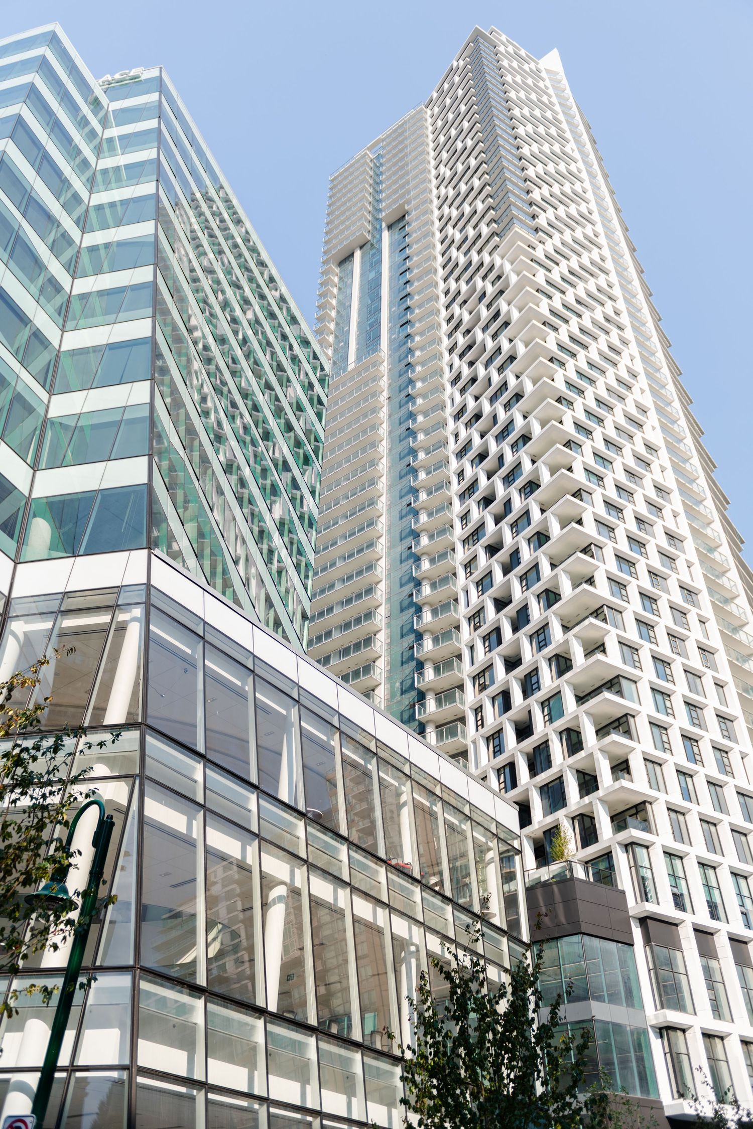 Looking up at a modern white high-rise tower with geometric balconies beside a glass office building.