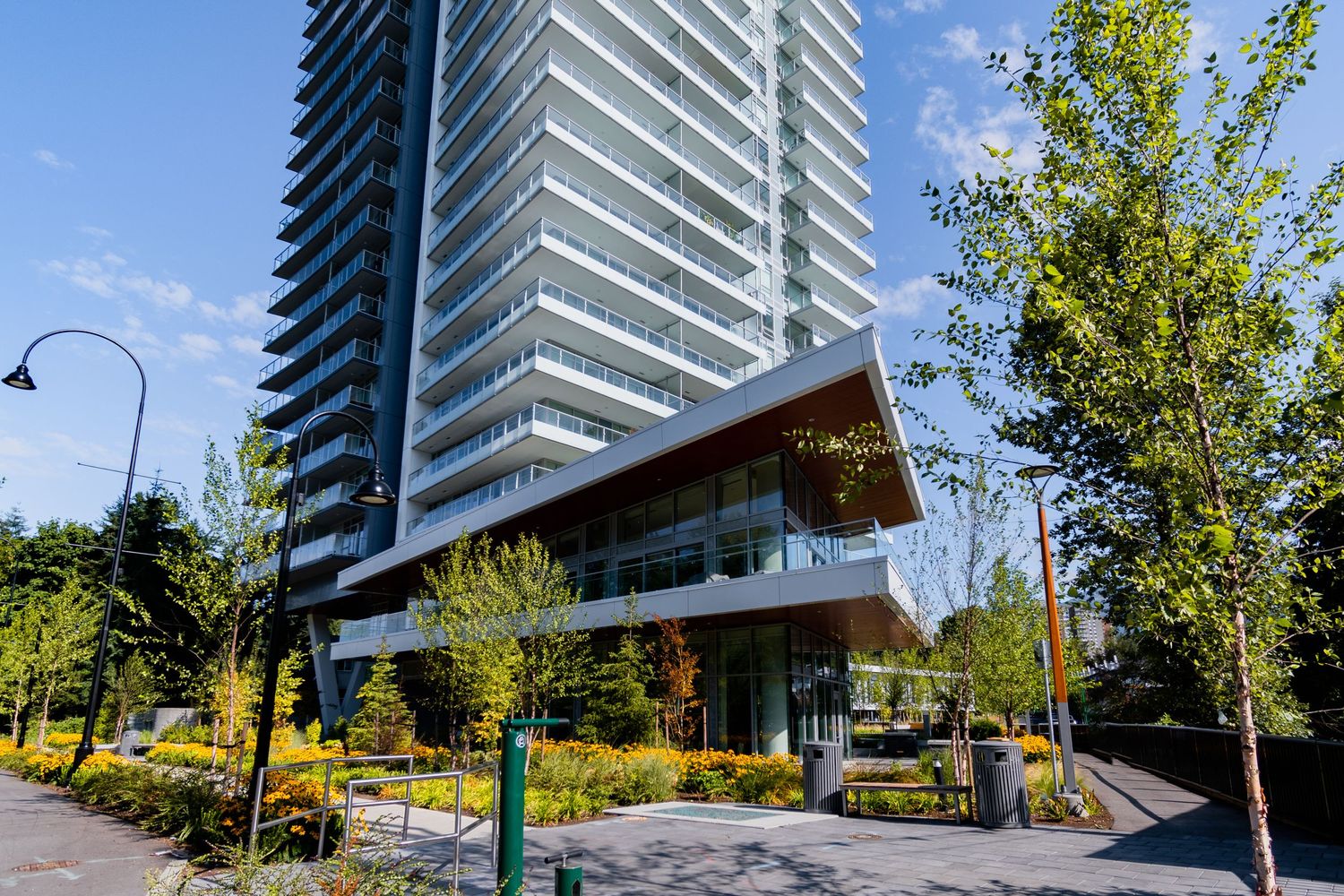 Modern glass residential tower with landscaped grounds and walking paths on a bright sunny day.