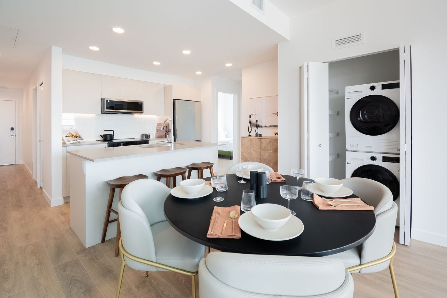 Bright modern kitchen and dining area with a black round table, white cabinetry, and stacked washer-dryer.