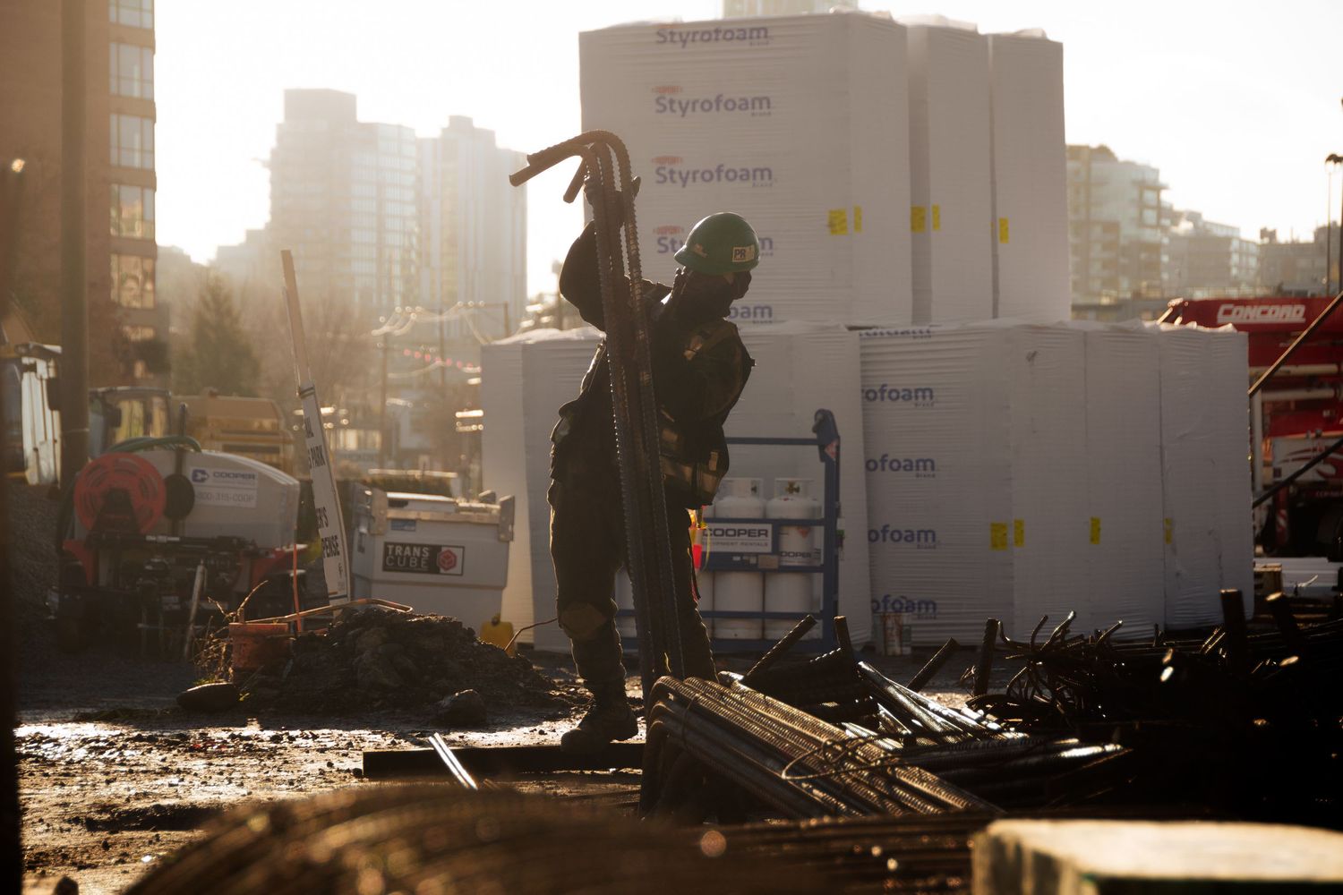 Construction worker carrying materials at an urban building site with Styrofoam insulation panels in background.