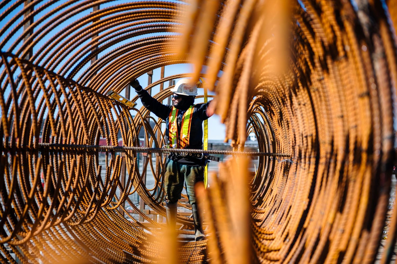 Construction worker framed through circular rebar cages at a large infrastructure project site.