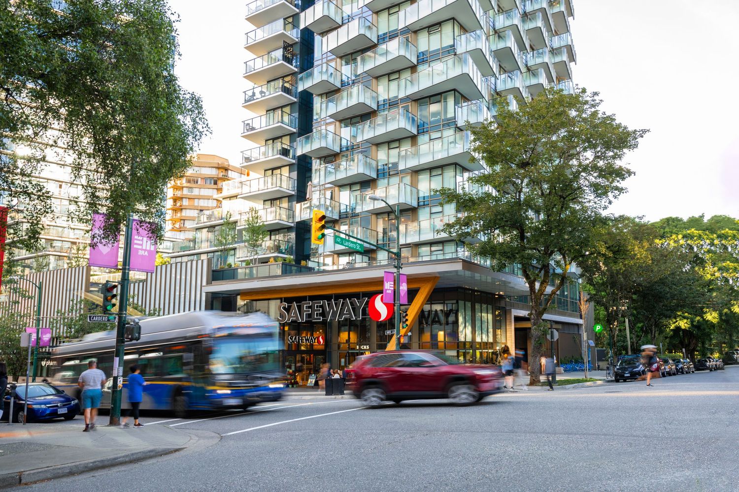 Busy urban intersection with Safeway store, transit bus, modern high-rise residential tower and street traffic.