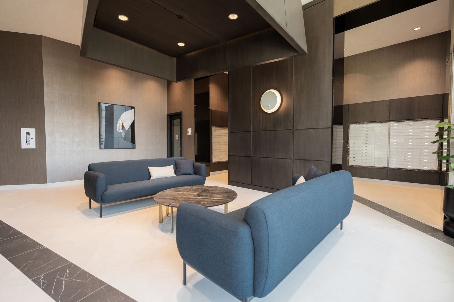 Modern building lobby with blue sofas, marble coffee table, and dark accent walls.