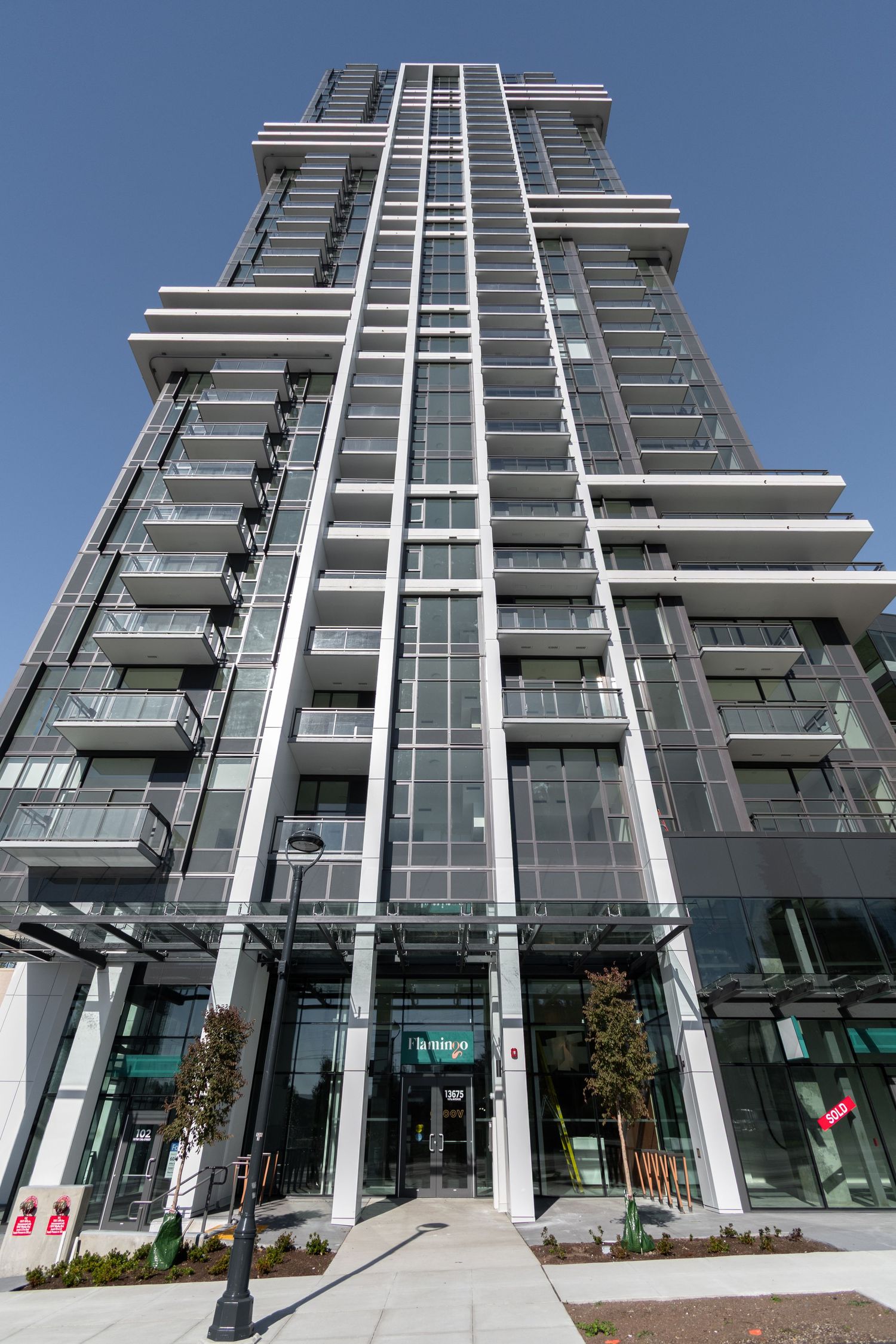 Tall modern glass and steel residential tower with balconies photographed from street level against blue sky.